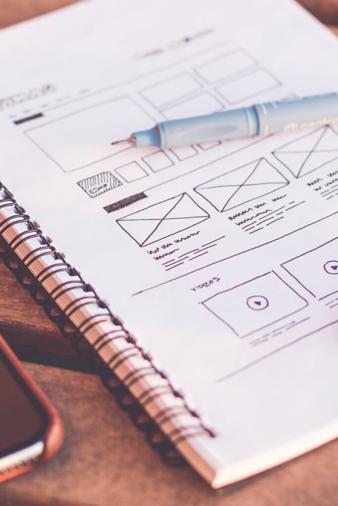 Close-up of a notebook with wireframe sketches and a smartphone on a wooden desk.